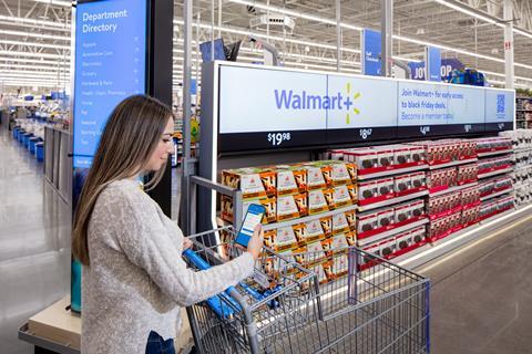 Woman entering Walmart story using her phone QR code and pushing empty trolley